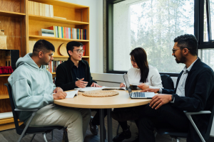 Students sit around a round table discussing literature against a backdrop of shelves filled with books