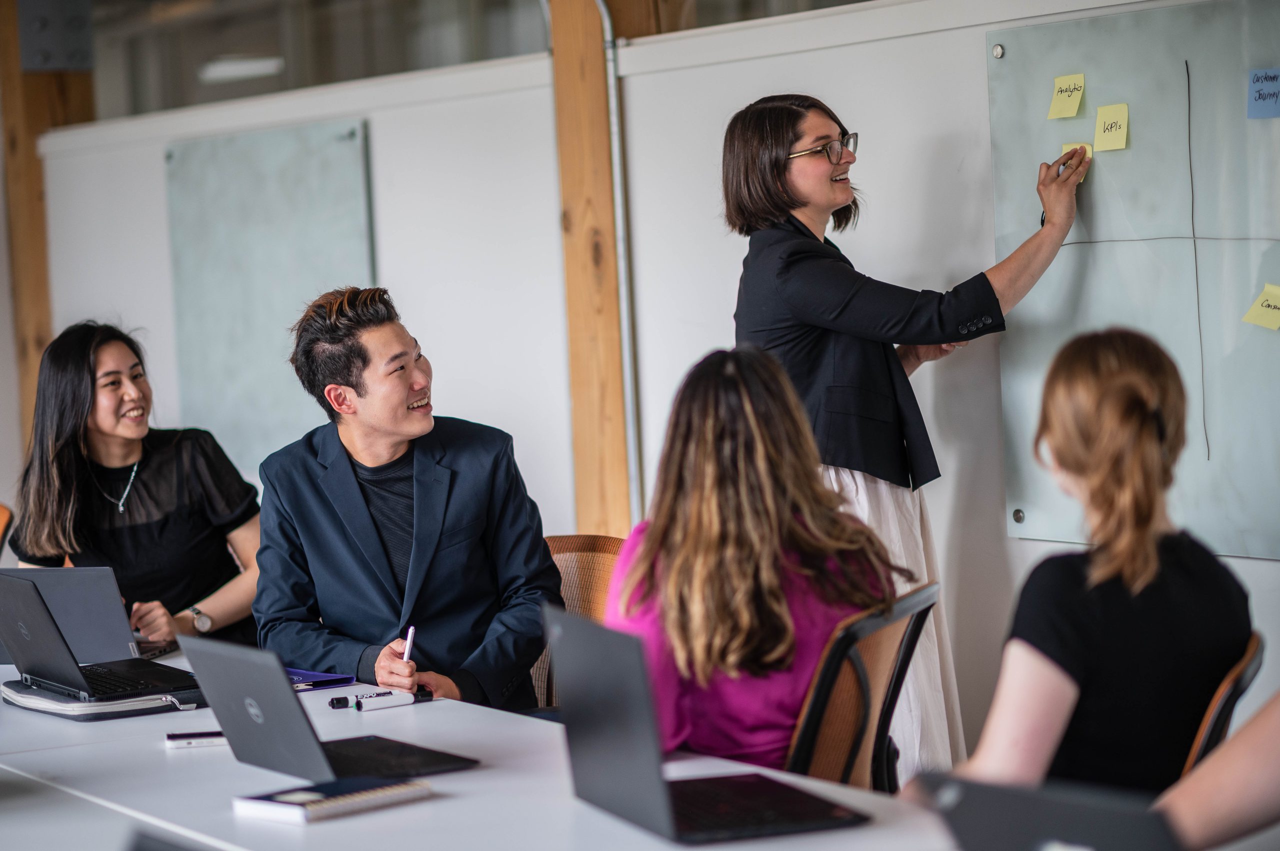 A student places notes on a whiteboard in a study room with a group of fellow students.