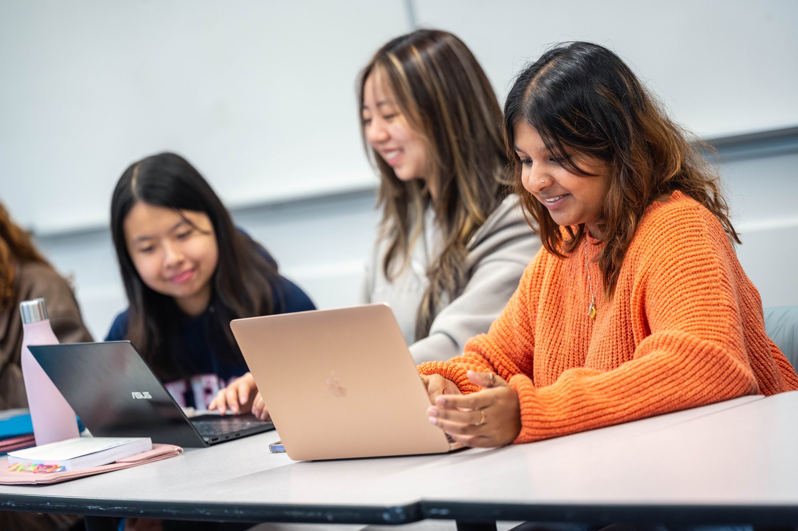 Three student in class at a table with their laptops.
