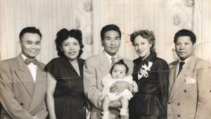 A black and white photo of five adults standing in formal attire with the man in the middle cradling a toddler.